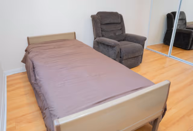 Small bedroom with a single bed, gray recliner, and a mirrored closet.