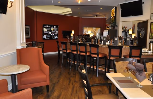 Interior dining and lounge area with a bar counter, high stools, tables and upholstered chairs in warm decor.