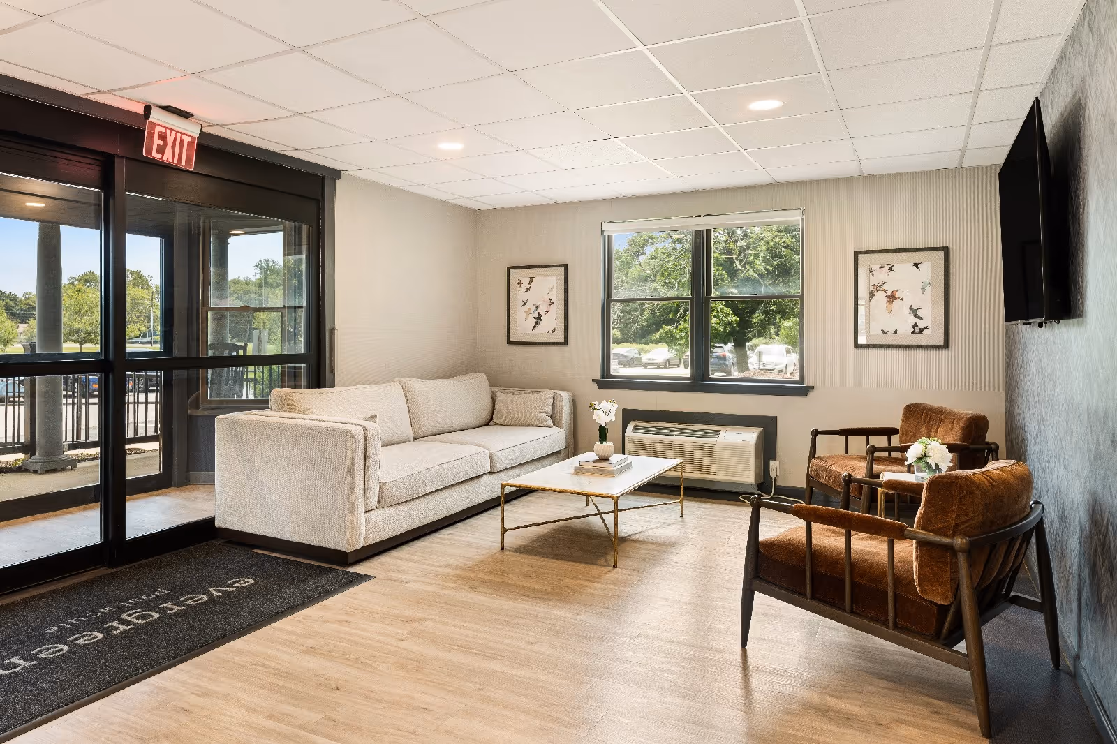Lobby seating area at Evergreen Post Acute with a sofa, two armchairs, a coffee table, and windows by the glass entrance.