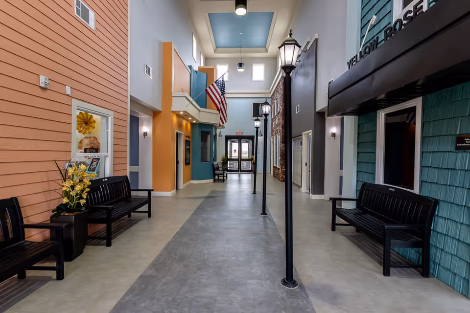Indoor hallway designed to resemble an outdoor street with building facades on either side, black benches, street lamps, an American flag, and a glass exit door at the end.