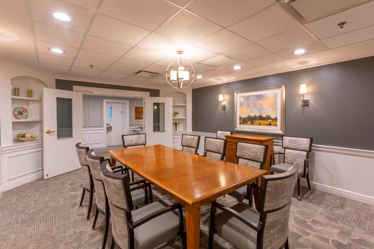Well-lit meeting/dining room with a long wooden table surrounded by upholstered chairs, wall art, and double doors.
