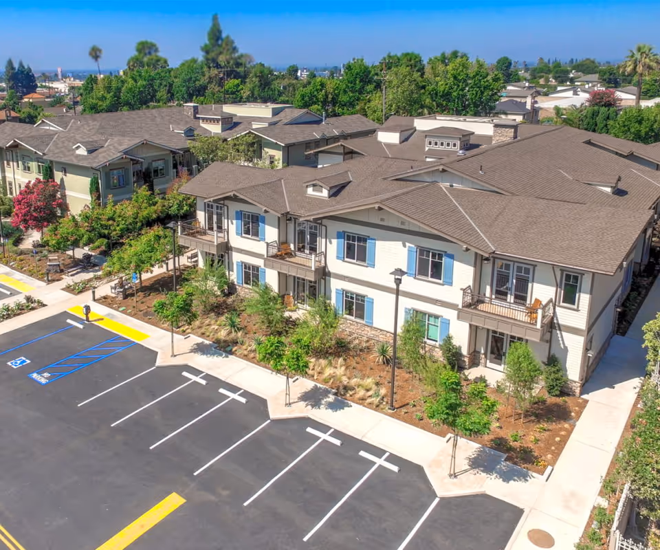 Aerial view of Santa Teresita Assisted Living Cottages showing beige, multi-unit buildings and surrounding parking lot.