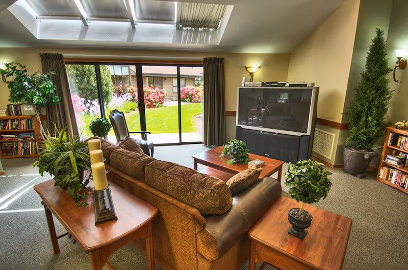 Communal living room with a sofa, coffee tables, large TV and sliding glass doors opening onto a garden.