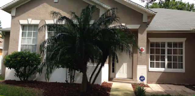 Front exterior of a senior living facility with palm trees and a doorway.