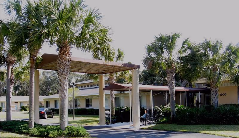 Exterior view of Fellowship Amelia Island facility showing a covered entrance with columns, surrounded by palm trees and greenery under a clear sky.