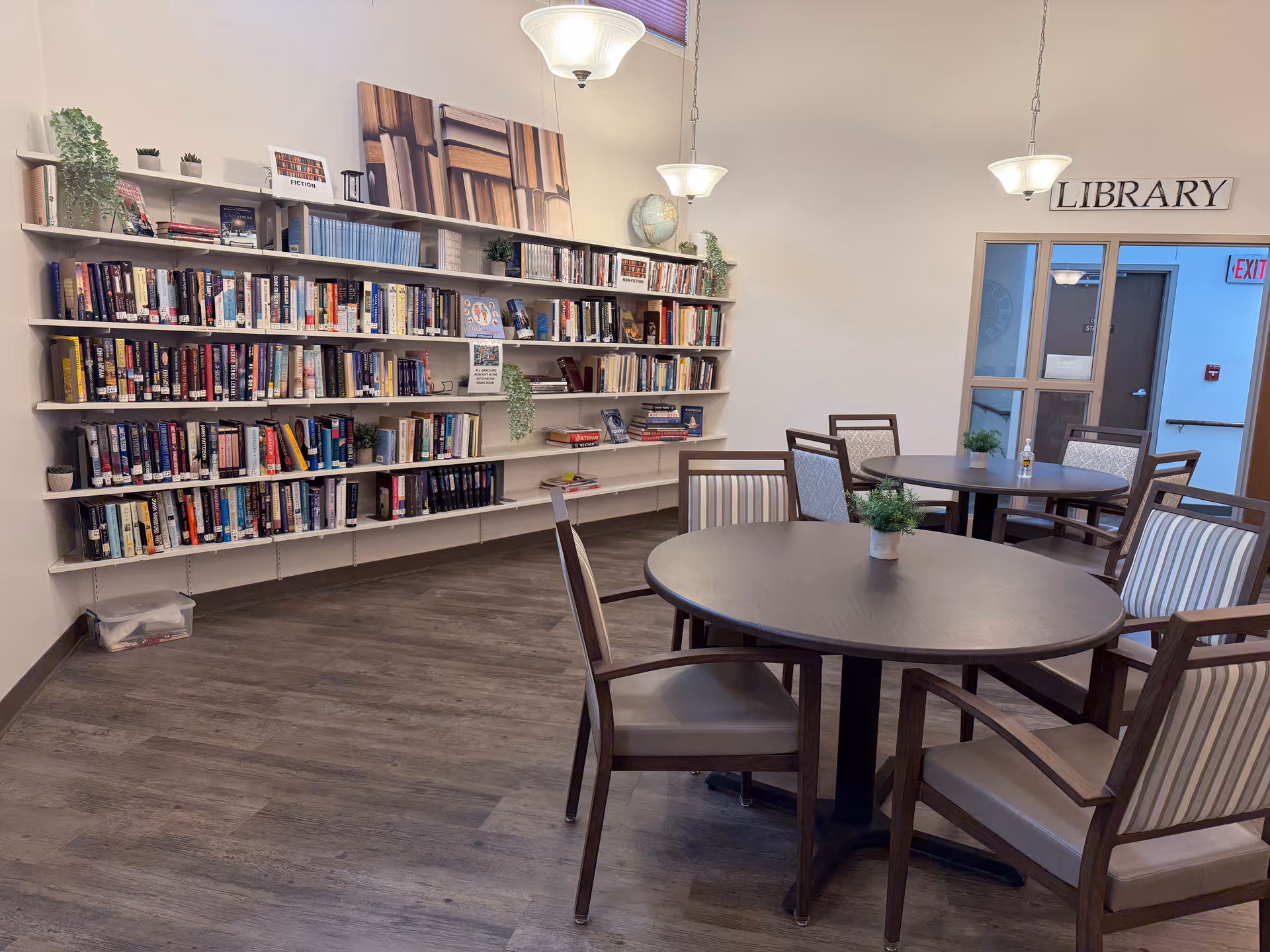 Interior of a small library with wall bookshelves and round tables with chairs.