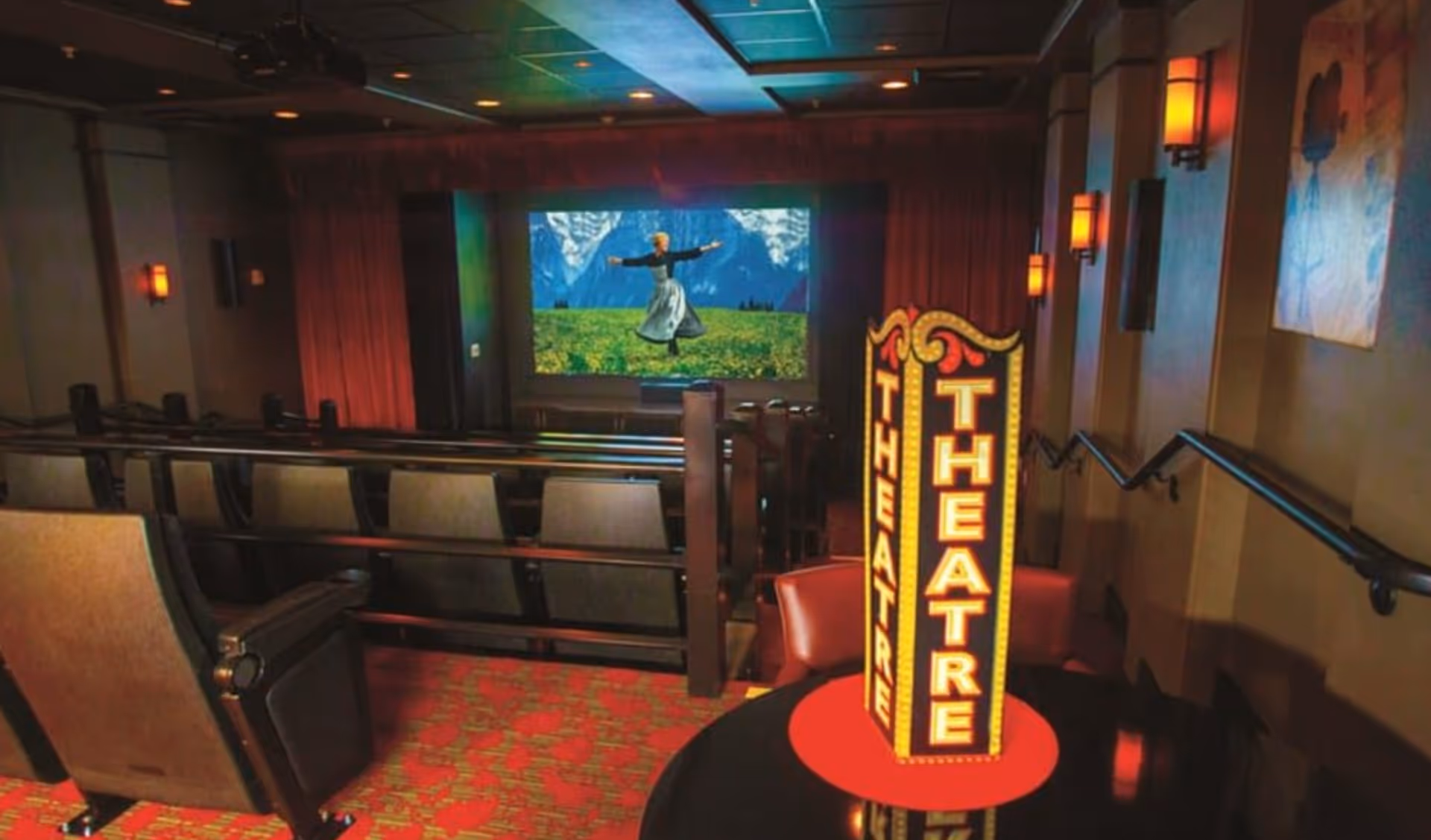 Small private movie theater with tiered seating, a screen showing a woman dancing in a meadow, and a lit 'THEATRE' sign on a table.