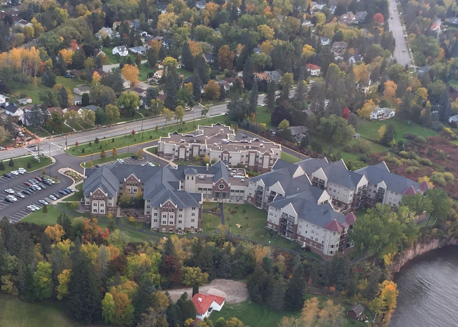 Aerial view of a large multi-building senior living complex surrounded by trees and a nearby body of water.