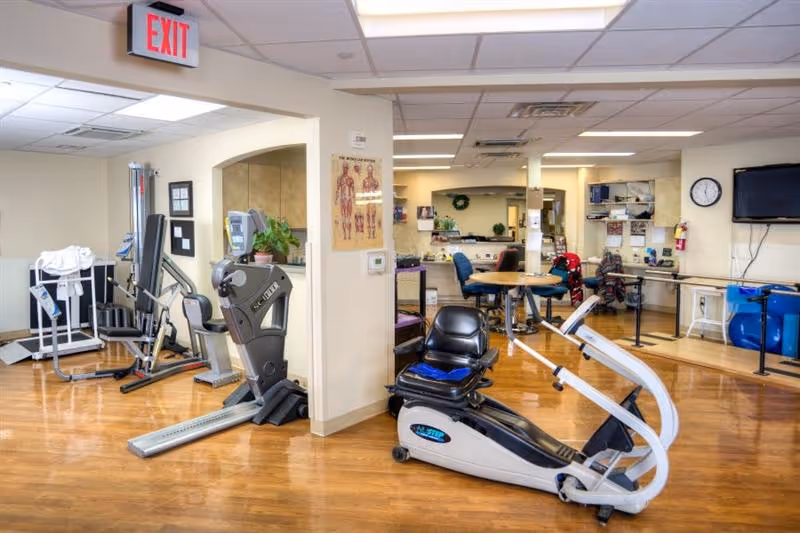 Bright interior rehabilitation/fitness room with exercise machines, therapy equipment, and seating.