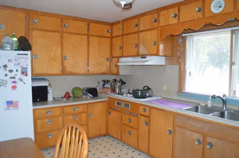 Compact wooden kitchen with upper cabinets, a stove, sink, and refrigerator.