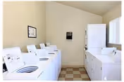Laundry room with white top-loading washing machines and stacked dryers along cream-colored walls and a checkered tile floor.