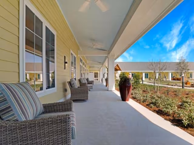 Covered porch with wicker seating and potted plants overlooking a landscaped courtyard.
