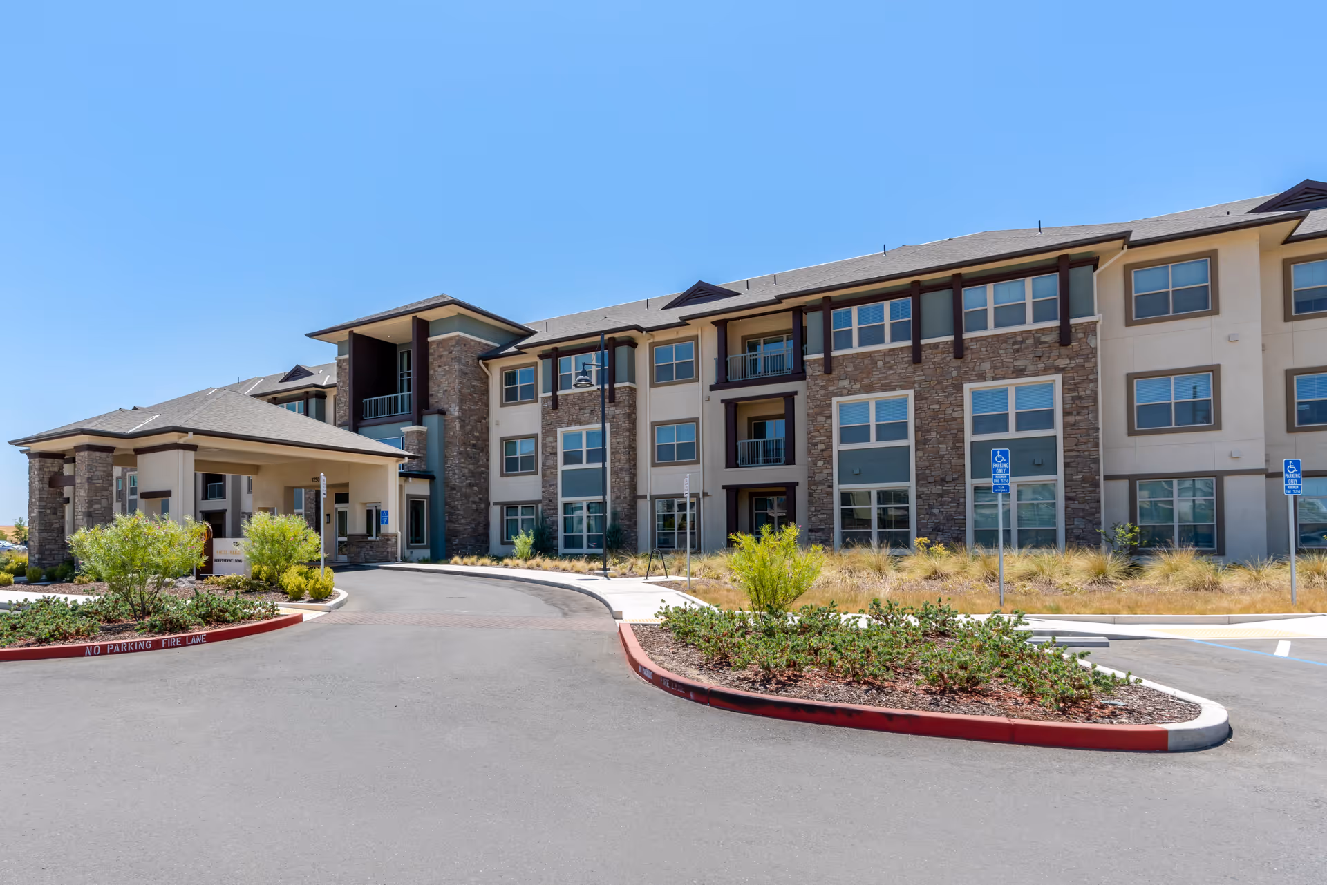 Front exterior of a three-story senior living building with a covered drop-off driveway and landscaped entrance.