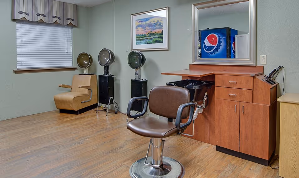 Interior salon with a styling chair, hair-washing sink, vintage hooded hair dryers, mirror, and cabinetry.