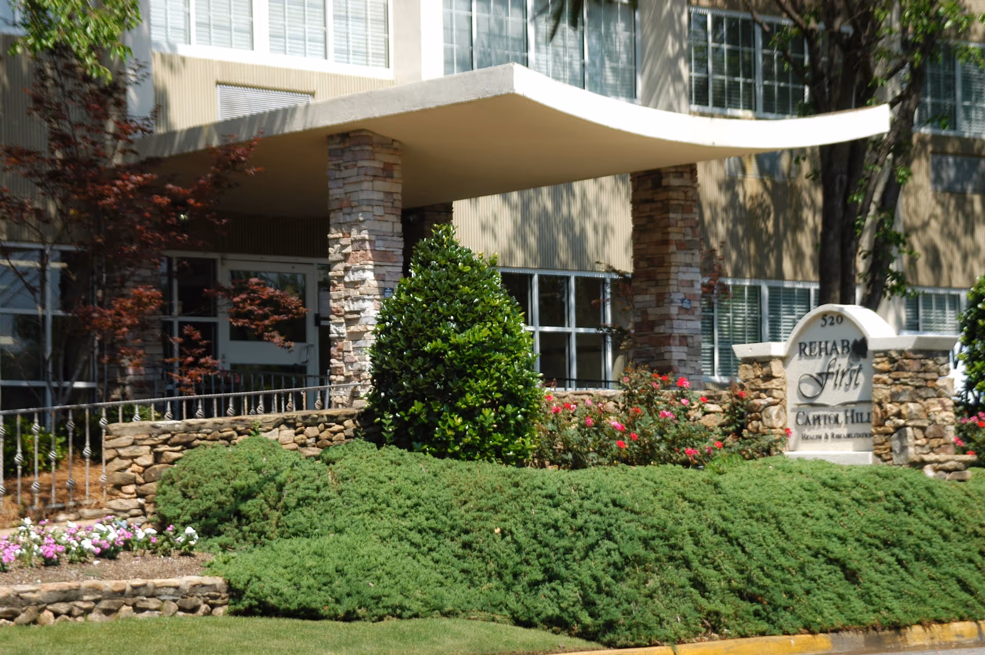 Stone-columned entrance and landscaped front sign reading 'Rehab First Capitol Hill' at a healthcare building.