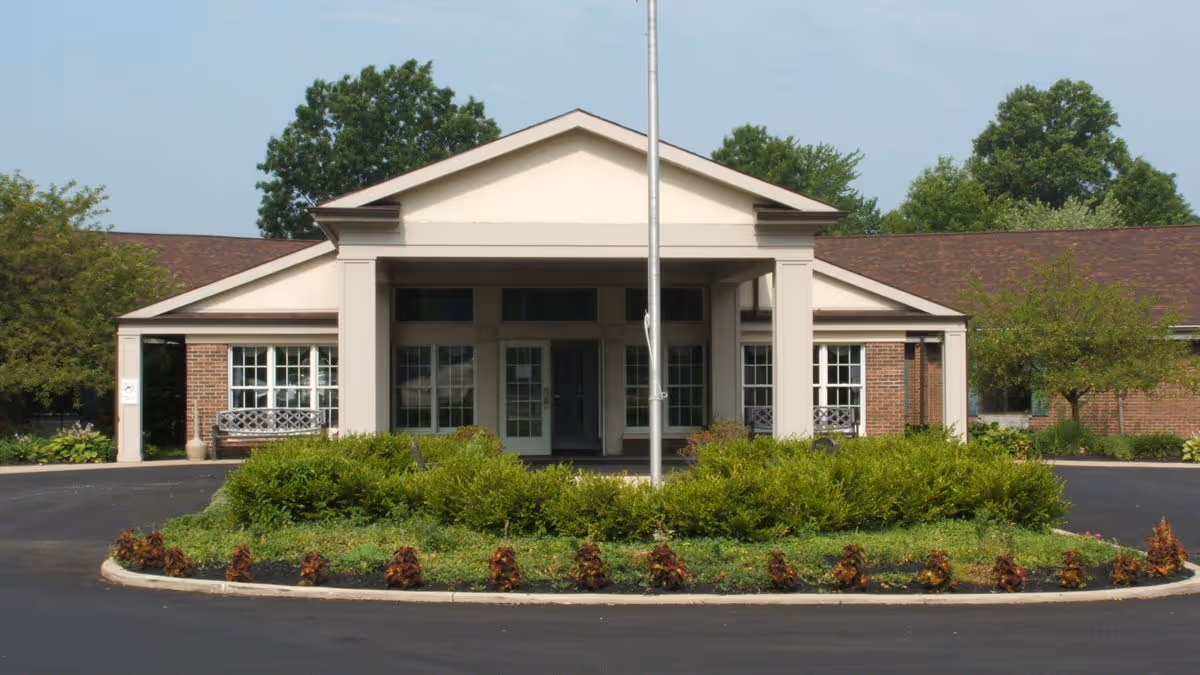 Front entrance of a single-story brick senior living facility with a covered portico, circular driveway, and landscaped island.