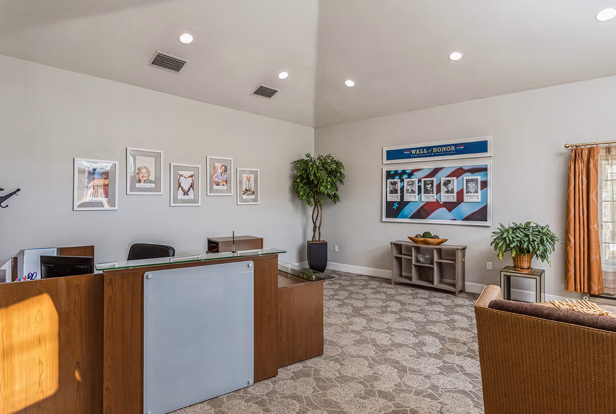 Reception area with a wooden front desk, framed portraits on the wall, potted plants, and a 'Wall of Honor' display.