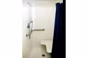 Accessible shower with blue curtain, grab bars, and a built-in bench in a bathroom.