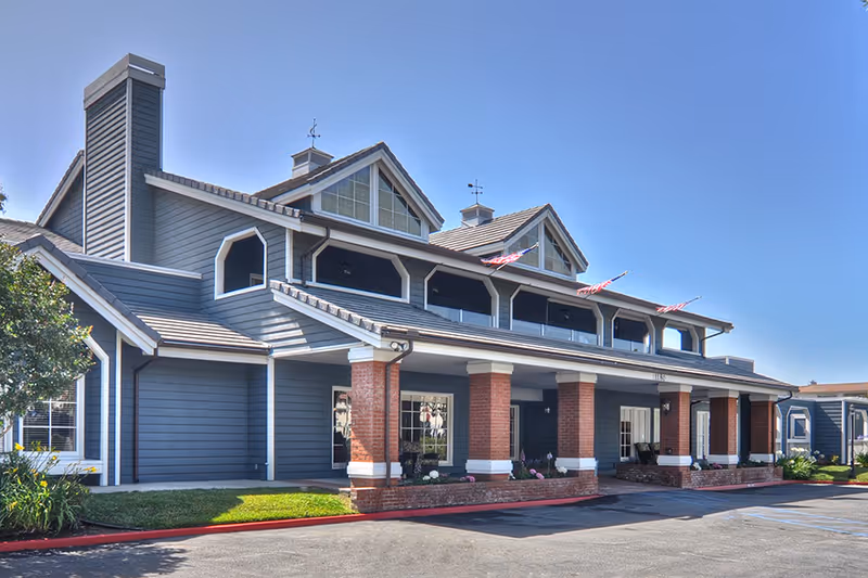 Blue-gray senior living facility exterior with brick columns and a covered entrance.
