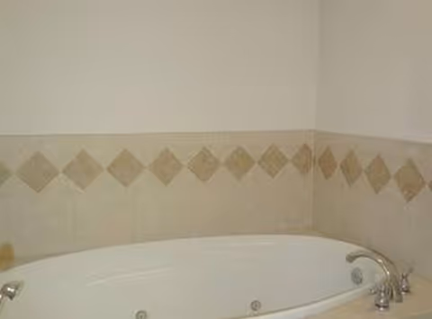 White jacuzzi tub in a tiled bathroom with beige diamond accents.