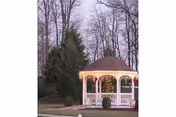 White gazebo decorated with string lights on a lawn with leafless trees in the background.