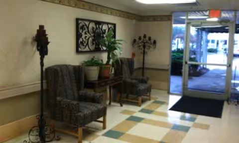 Lobby seating area with patterned chairs, plants, lamps, and glass entrance door.