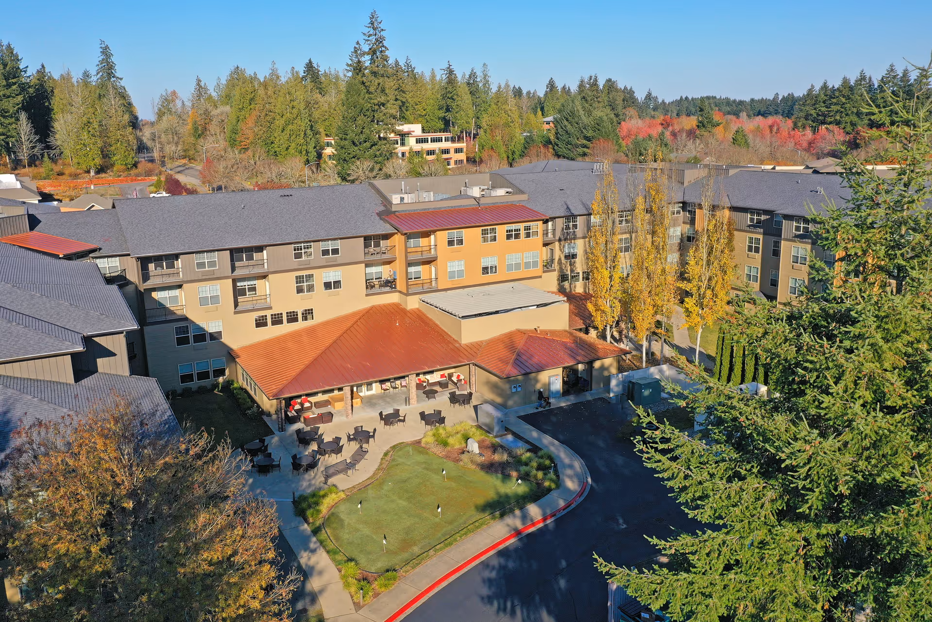 Aerial view of the Bonaventure of Lacey senior living building with an outdoor patio, small putting green, and surrounding trees.