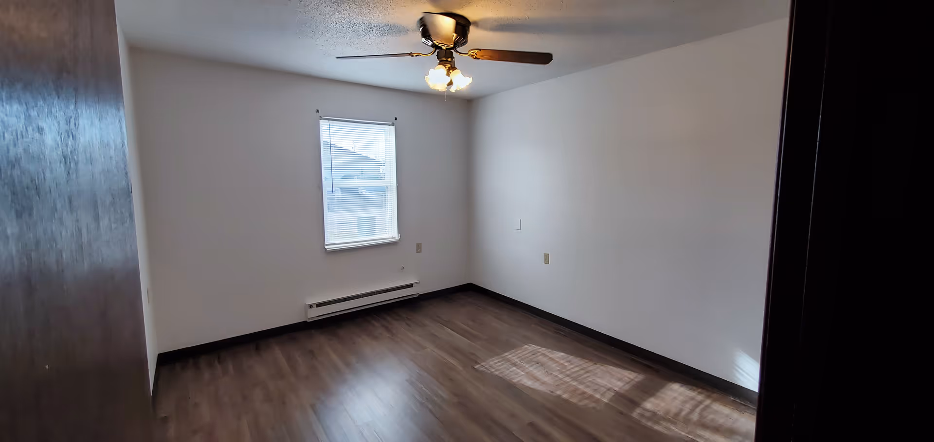 Empty bedroom with white walls, wood-look flooring, a ceiling fan, and a single window.