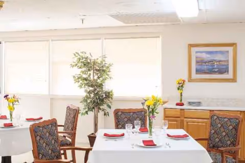 Bright dining room with tables set in white tablecloths, flowers, and framed artwork.