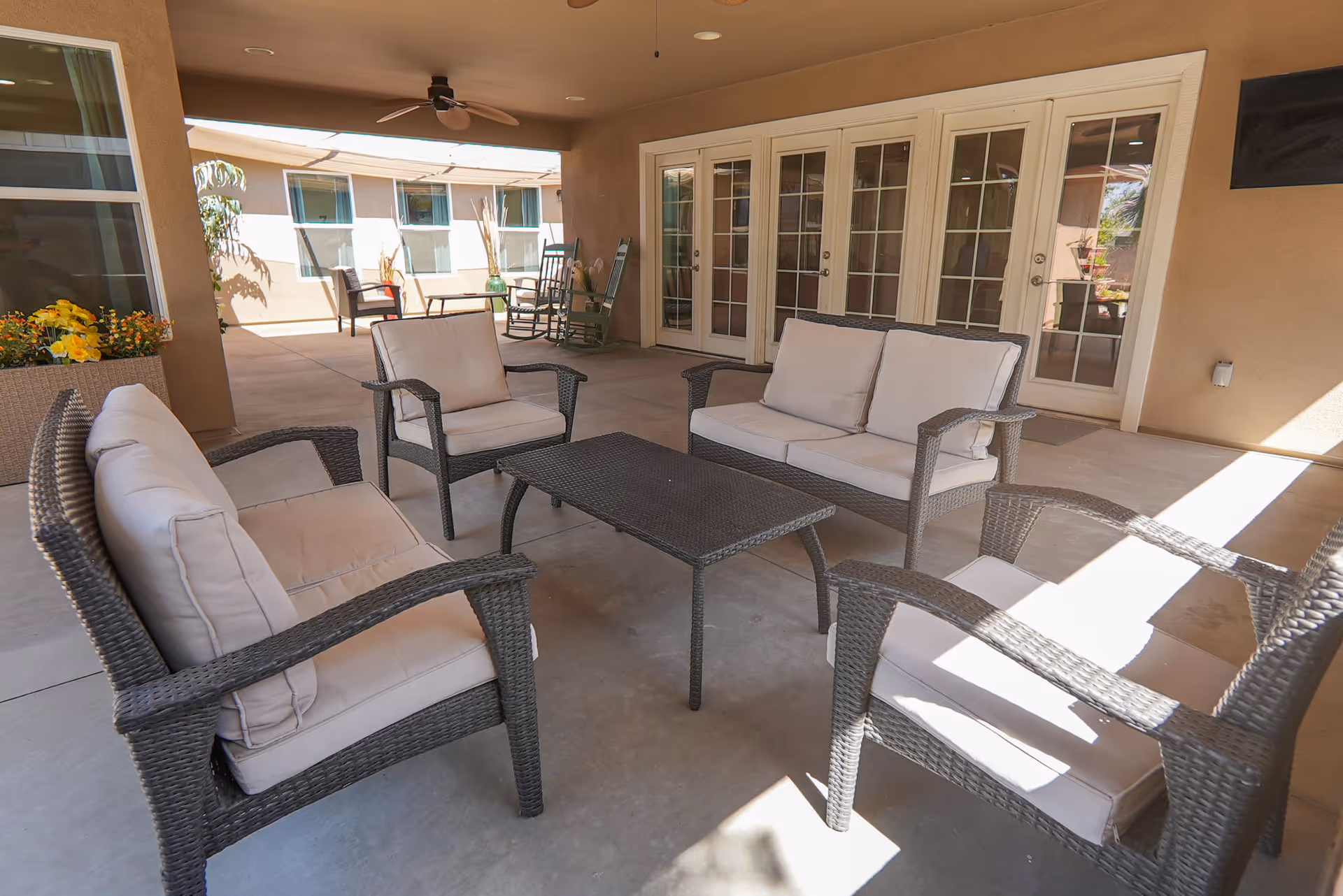 Covered outdoor patio with wicker seating and a central coffee table in front of glass French doors.