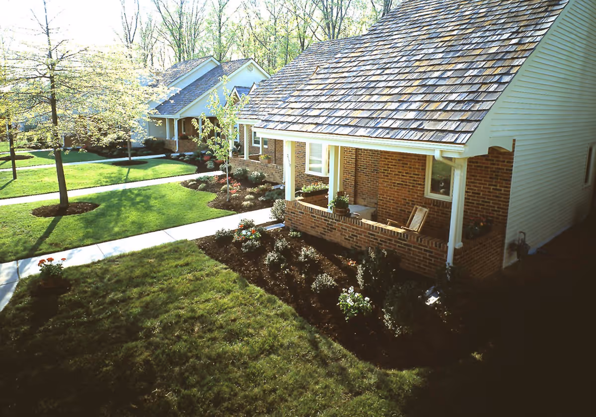 Single-story brick cottages with covered porches, landscaped lawns, and walkways in a residential community.