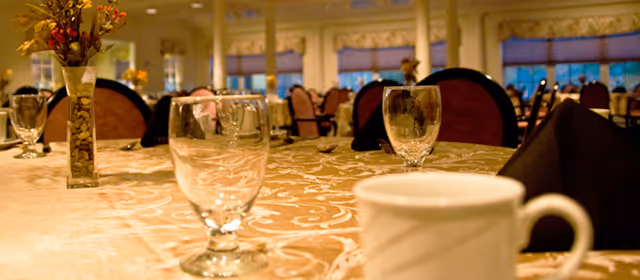 Close-up of a decorated dining table with glassware, a coffee cup, black napkins and a floral centerpiece in a large dining room.