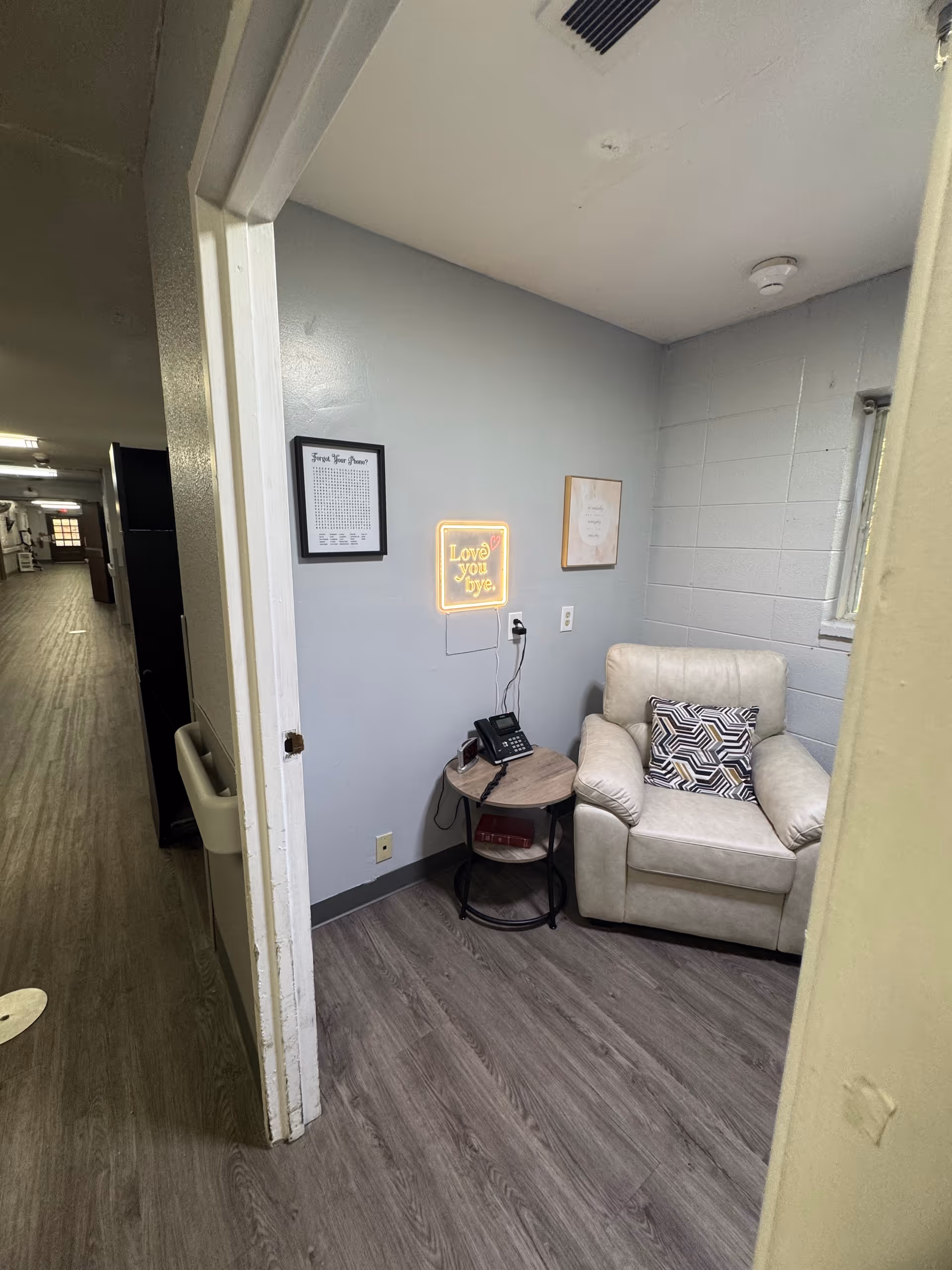 A small seating area with a chair, a side table, and a wall sign in a senior living facility.