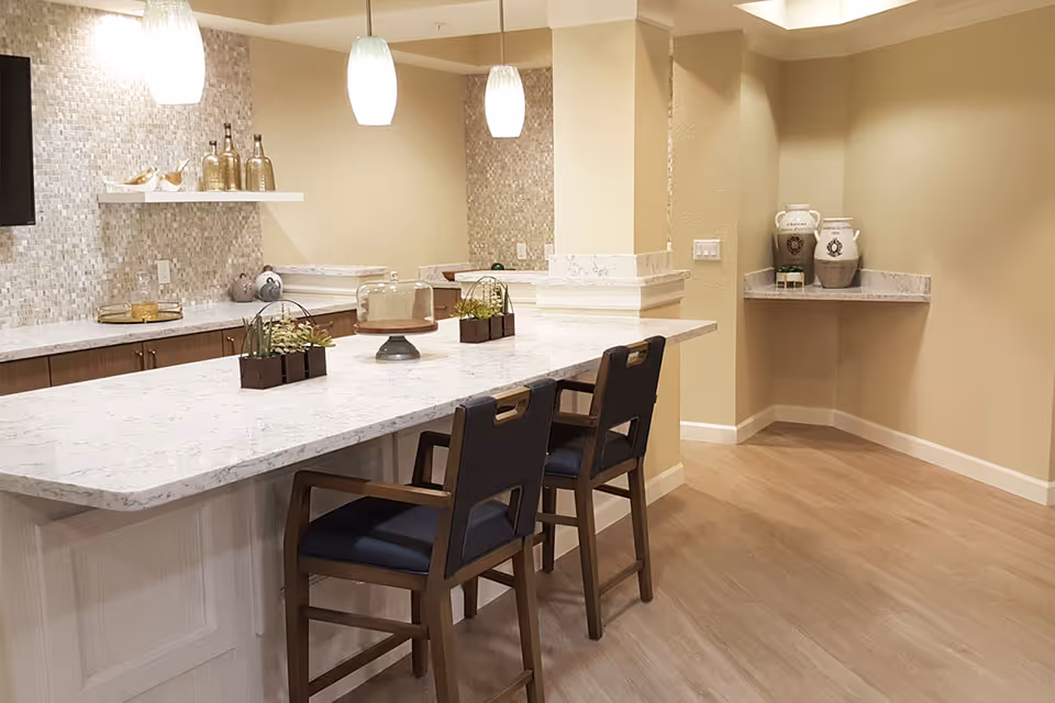 Bright communal kitchen area with a marble-topped island, pendant lights, decorative accents, and two bar stools.