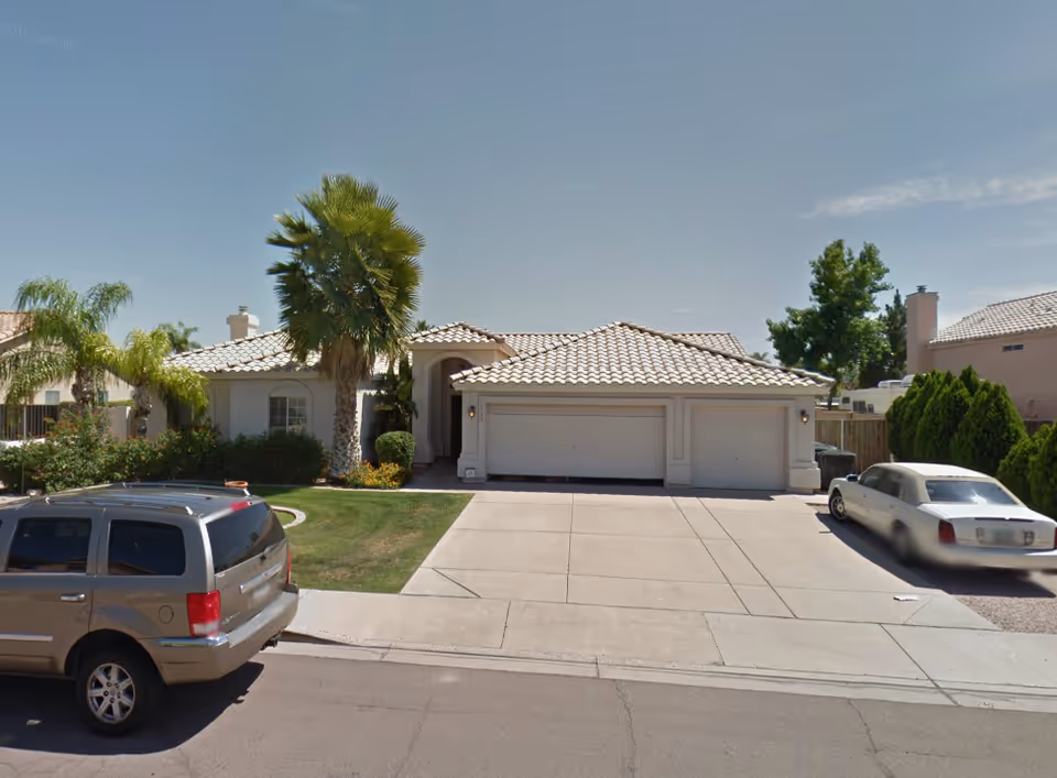 Residential home with a three-car garage, tile roof, palm trees, and a curved driveway.