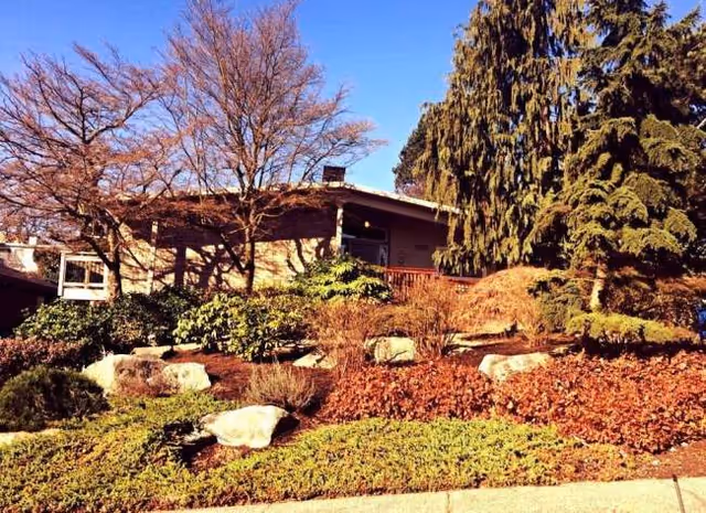Exterior view of a single-story building with landscaped hillside, trees, and rocks.