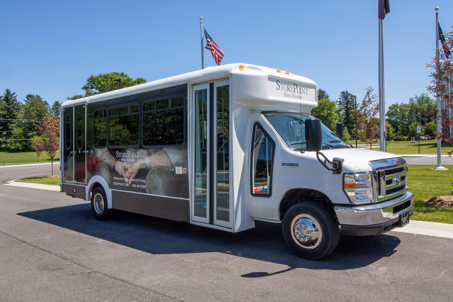 A StoryPoint shuttle bus parked on a driveway outside with flags and trees in the background.