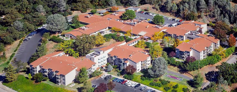 Aerial view of Auburn Ravine Terrace senior living campus showing multiple connected buildings with red roofs, parking lots, and landscaped trees.