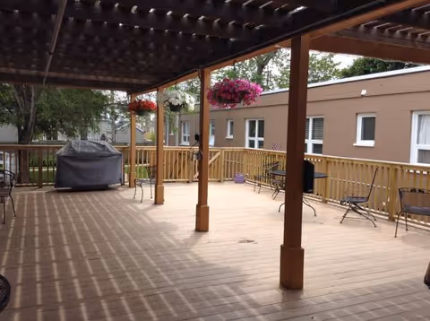 Wooden outdoor deck with hanging planters and seating beside a brown building.