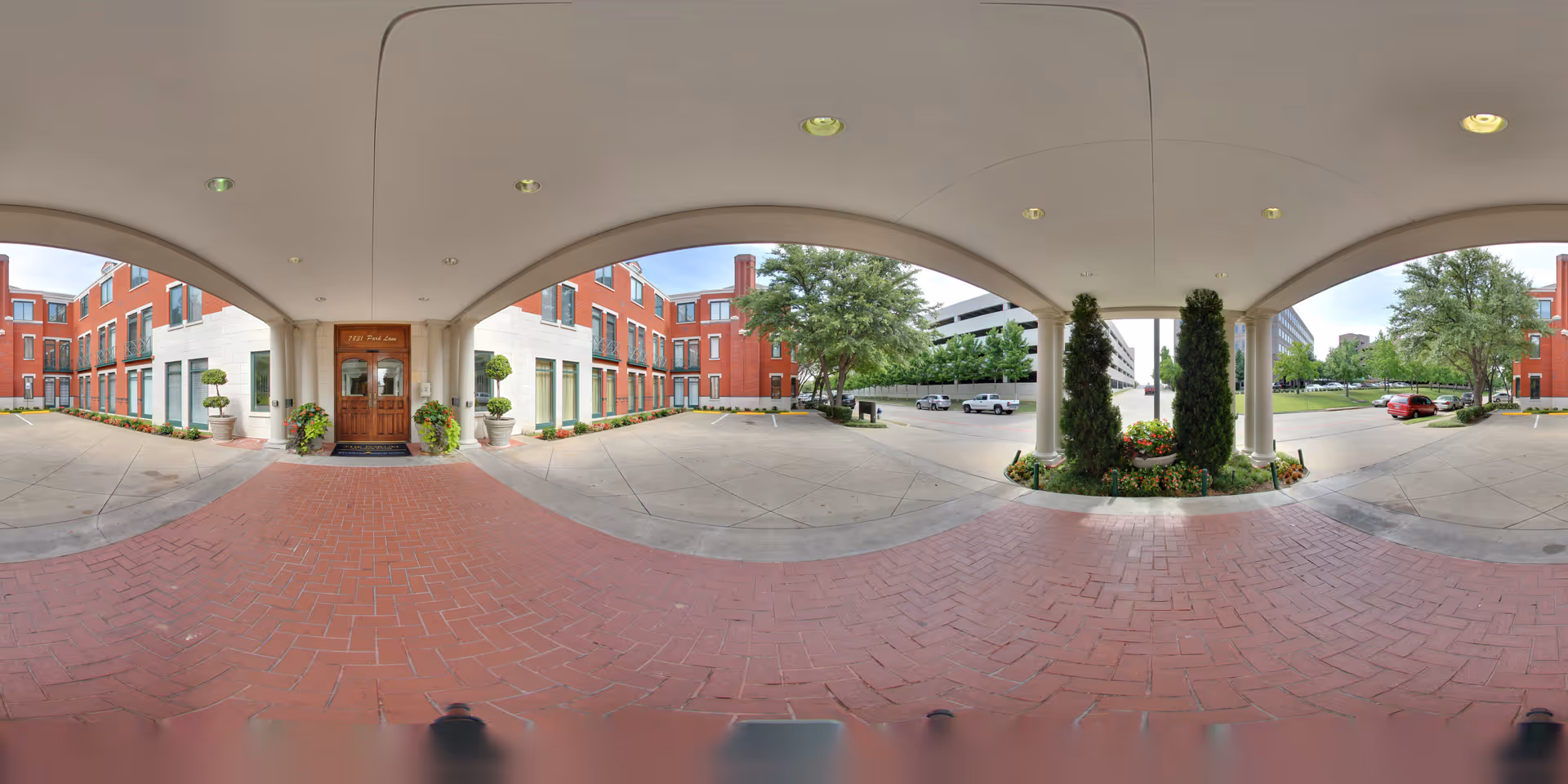 Covered porte-cochère entrance to a red-brick building with columns, planters, and a driveway.