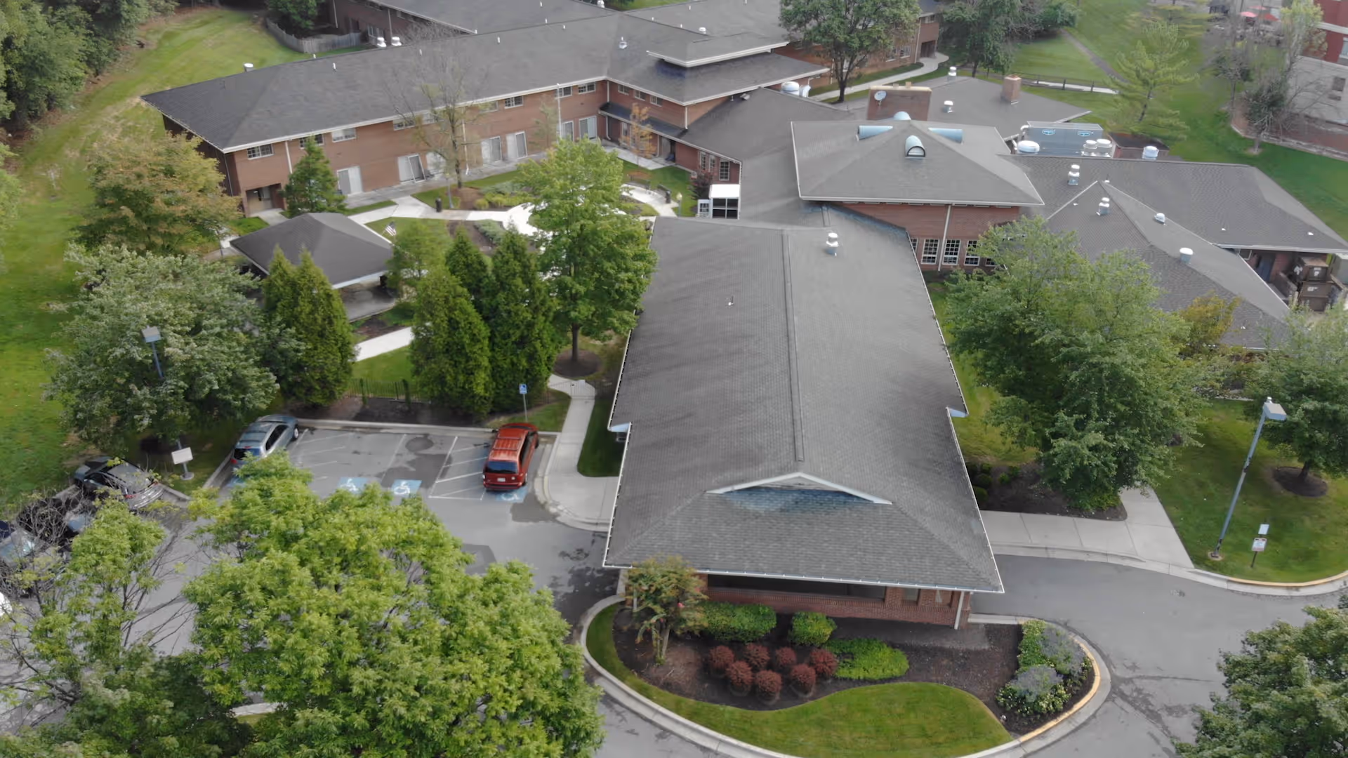 Aerial view of Layhill Nursing And Rehabilitation Center showing multiple connected buildings with gray roofs surrounded by green trees, landscaped bushes, and parking spaces including handicapped spots.