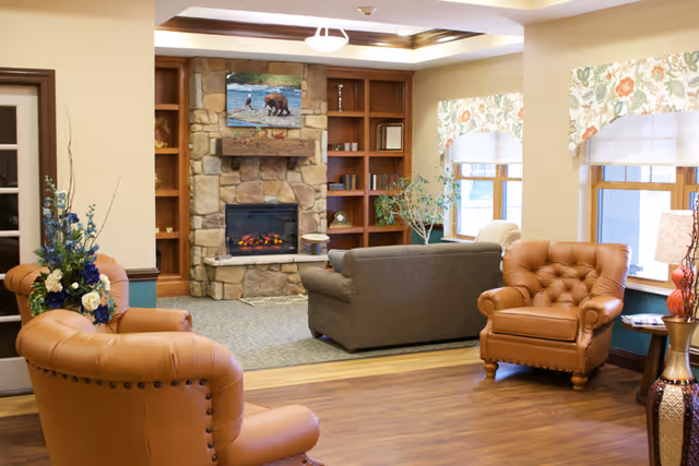 A comfortable sitting area with leather armchairs and a sofa facing a stone fireplace and built-in shelving by windows.