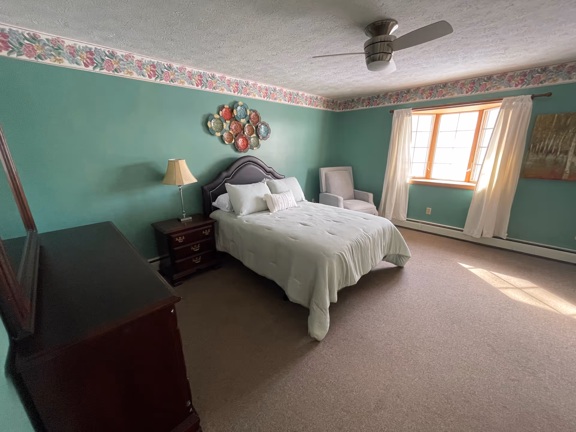 Bright bedroom with a bed, nightstands, dresser, armchair, green walls and a window with curtains.