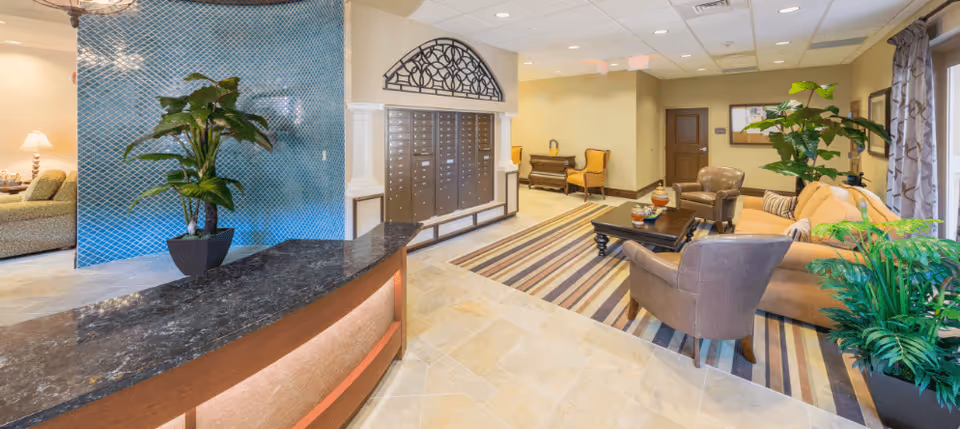 Bright reception lobby with a curved front desk, seating area, mailboxes, and potted plants.