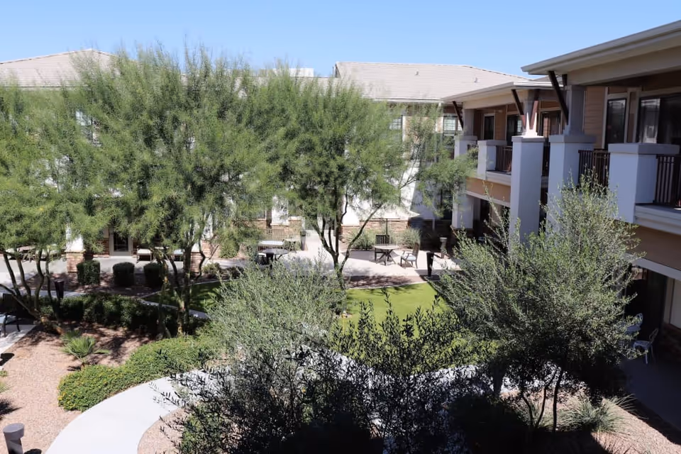 Landscaped inner courtyard with trees, lawn, walkways, seating areas, and surrounding two-story residential building.