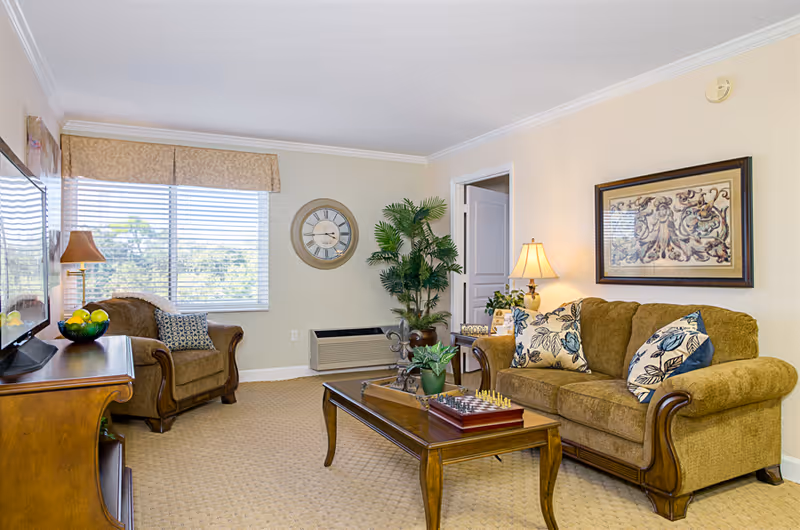 Cozy furnished living room with a sofa, armchair, coffee table, TV console, and window with blinds.