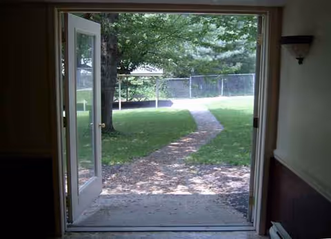 Door opens to a grassy backyard with a path, trees, and fence.