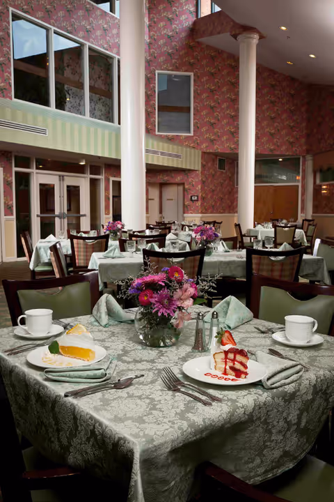 A dining room with tables set with green tablecloths, floral centerpieces, cups, and plated desserts.