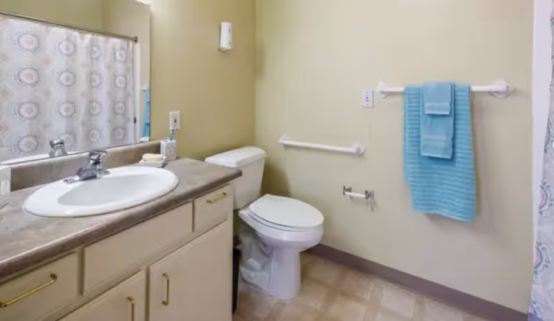 A clean bathroom with a white sink and countertop, a toilet, a towel rack with blue towels, and a shower curtain with a circular pattern.