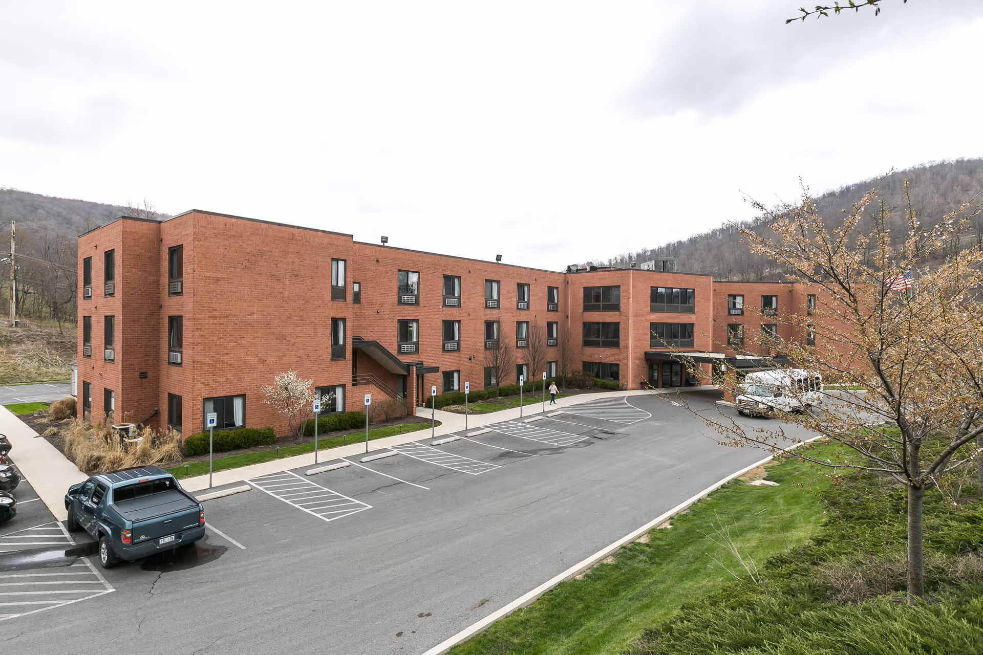 Front exterior of a three-story red brick nursing and rehabilitation building with a driveway, parking lot, and entrance canopy.